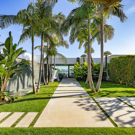 Modern walkway with palm trees and green lawn under clear blue sky.