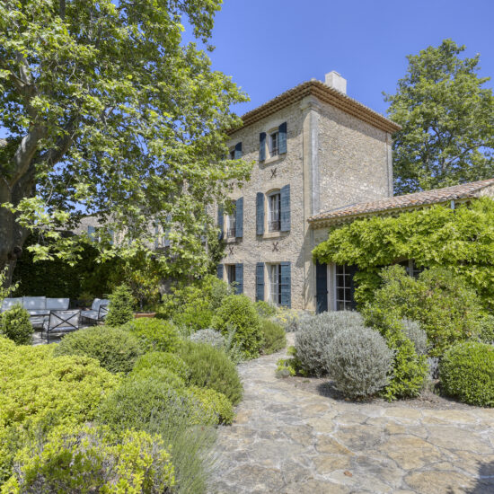 Charming stone house surrounded by lush greenery on a sunny day.