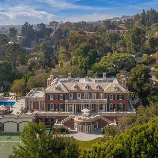 A grand mansion surrounded by lush greenery and hills under a blue sky.