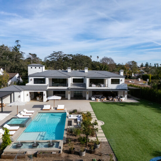 Modern white house with a large pool and expansive green lawn under a blue sky.