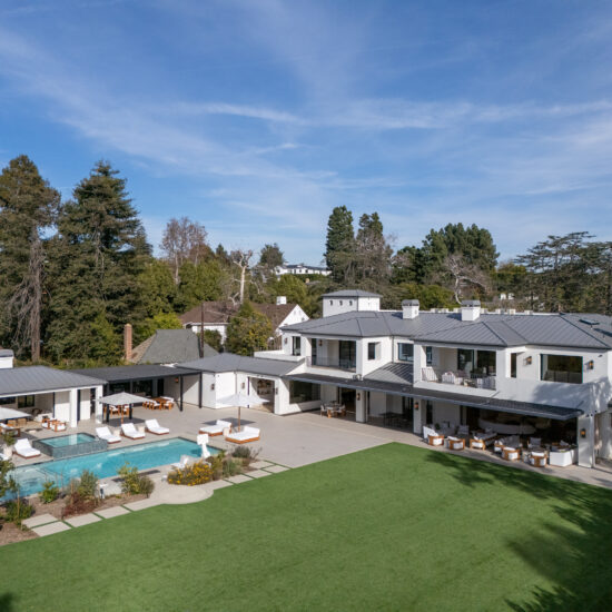 Luxurious modern mansion with a pool and spacious lawn under a clear sky.
