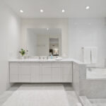 Modern white bathroom with a large mirror and marble accents.