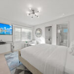 Bright, modern bedroom with white decor and large windows.