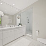 Bright white modern bathroom with glass shower and double sinks.