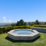 Octagonal stone hot tub on green lawn with clear blue sky.
