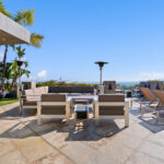Modern outdoor seating area with beige sofas and a fire pit under a clear blue sky.
