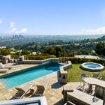 Luxury pool and hot tub overlooking a city skyline under a clear blue sky.