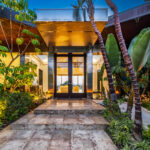 Modern home entrance with glass doors and tropical landscaping.