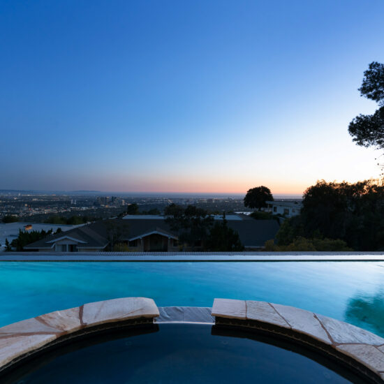 Infinity pool overlooking a city at sunset with clear sky.